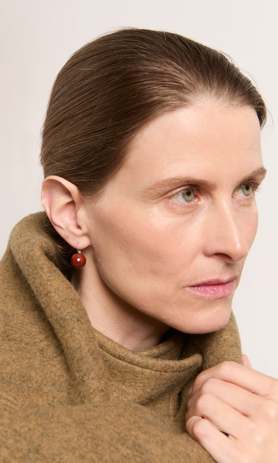 Plümo  Woman with brown hair in a brown coat wears Terra Earrings, looking thoughtfully to the side.