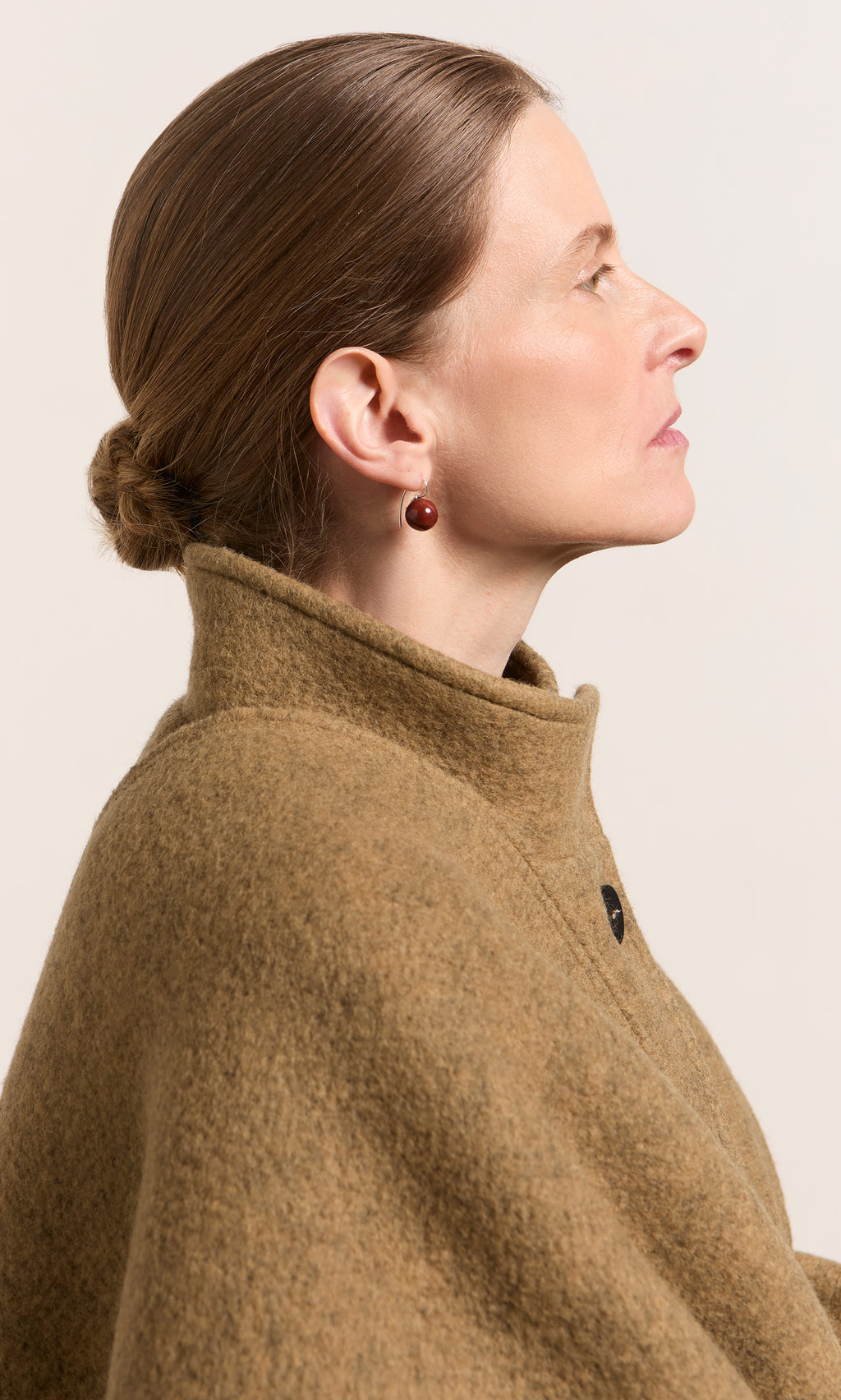Plümo  Woman in profile with brown hair in a bun, brown coat, and Terra Earrings, looking to the right.
