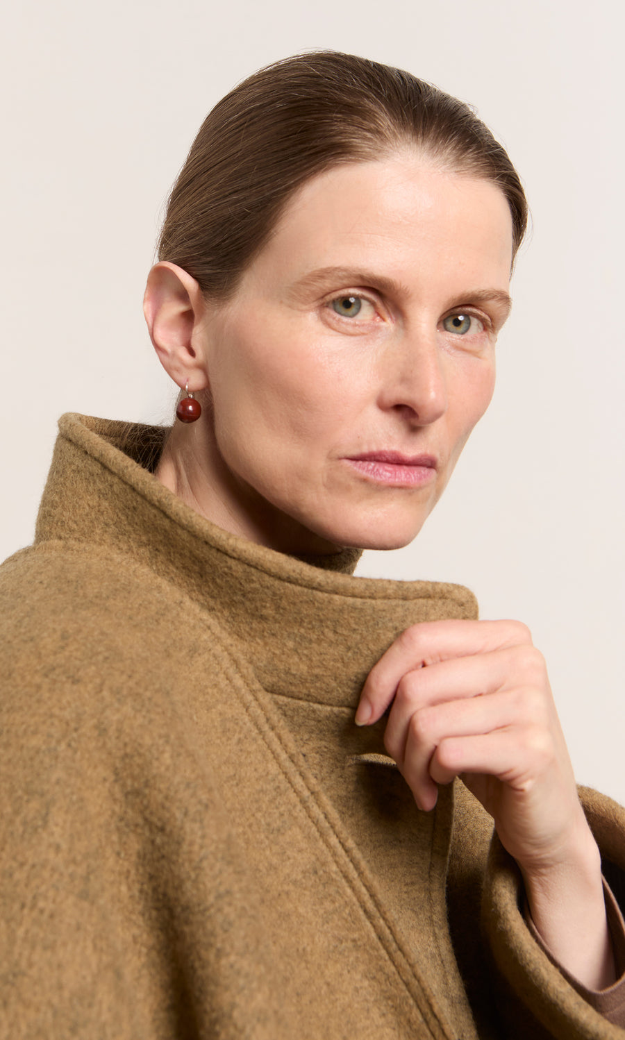 Plümo  Woman with light skin and brown hair wears a brown coat and Terra Earrings, looking seriously at the camera.
