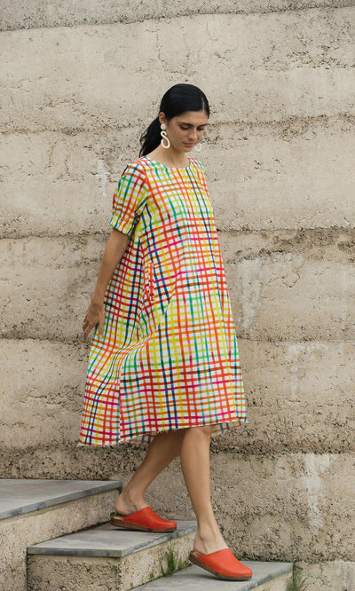 Plümo- Woman in the Thea Dress and red shoes walks down steps against a textured concrete wall.