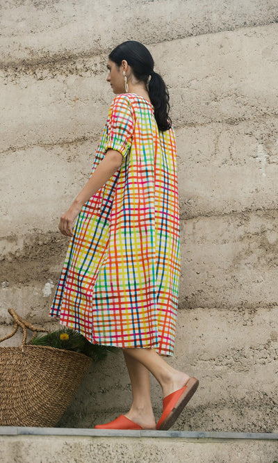 Plümo- Woman in the hand-dyed Thea Dress walks up steps, wearing orange shoes and carrying a woven basket of flowers.