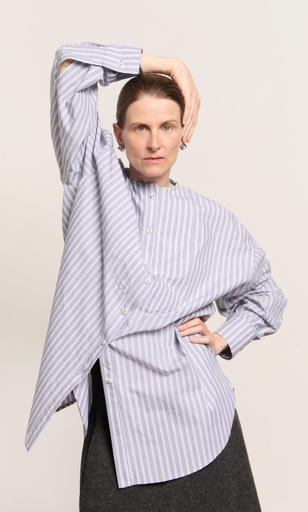 Plümo  Woman in a chambray blue Tuxedo Shirt poses confidently, hand on head, looking at the camera.