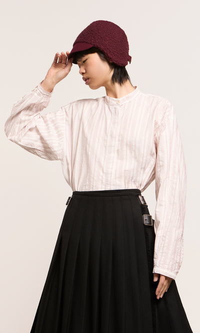 Plümo  Model wears loose white striped shirt, black skirt, and maroon Velo Wool Cap with ear flaps against a plain background.