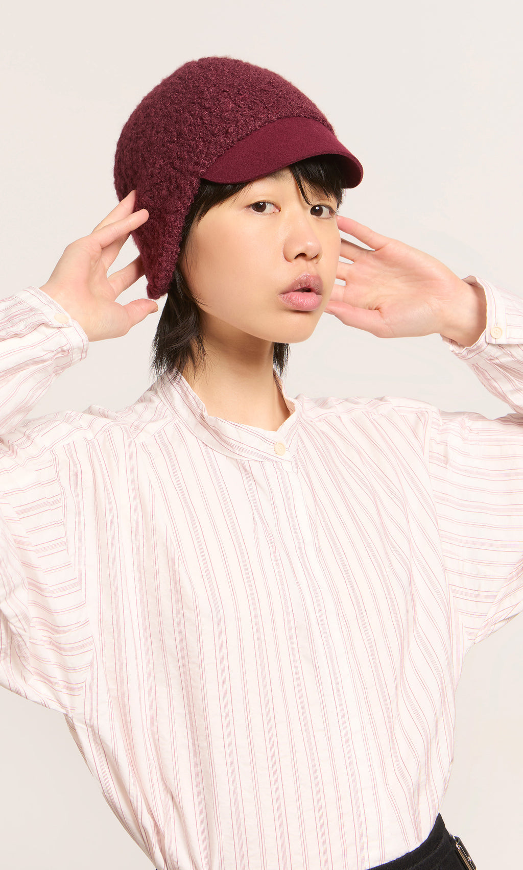 Plümo  Person in a striped shirt and Velo Wool Cap poses playfully against a light background.