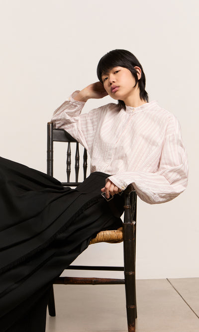 Plümo  Person in a Velo Wool Cap sits sideways on a wooden chair, leaning back with a relaxed expression.
