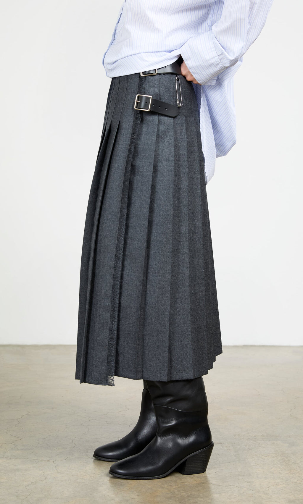 Plümo- Wearing the Boyd Kilt in grey worsted wool with side buckles, black boots, and a light blue shirt indoors.
