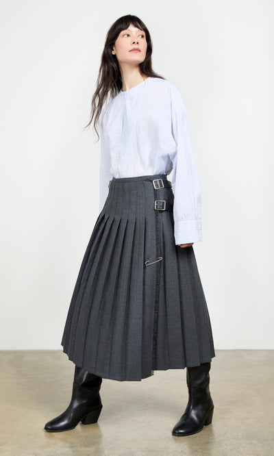 Plümo- Woman in a light blue blouse, Boyd Kilt with buckles, and black boots stands on a concrete floor.