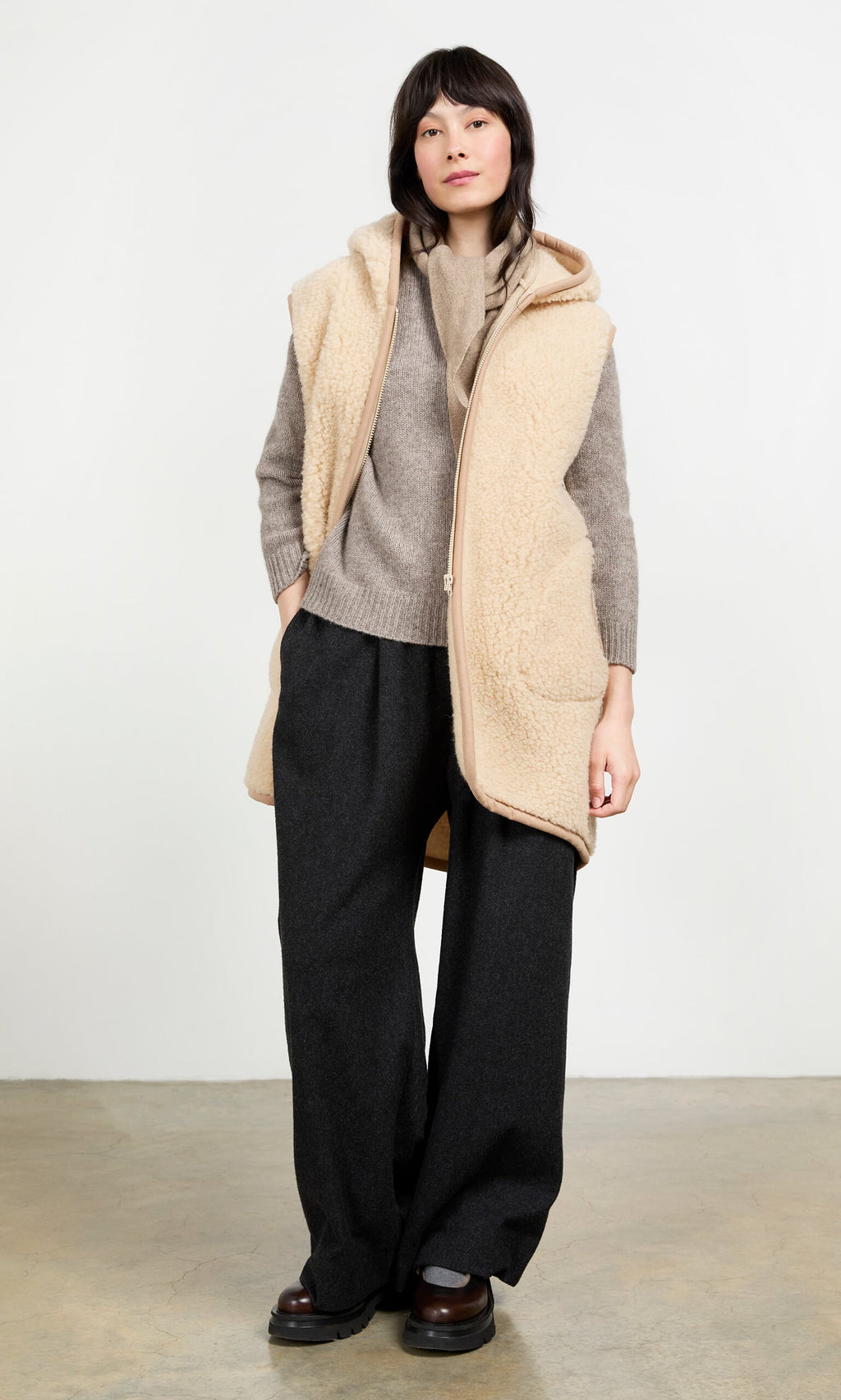 Plümo- Woman wears the Long Rambler Gilet - Natural with a gray sweater, wide-leg dark pants, and brown shoes.