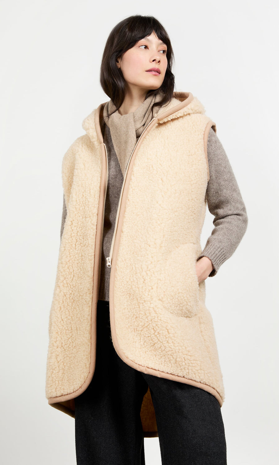 Plümo- Woman wears the Long Rambler Gilet - Natural over a gray sweater and black pants, hand in the gilet pocket.