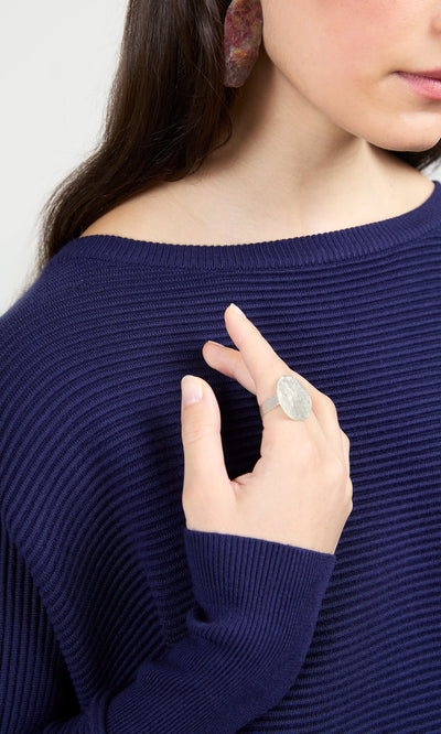 Plümo- Woman in a navy ribbed sweater wearing the Eco Silver Pebble Ring and colorful earrings, shown from shoulders up.