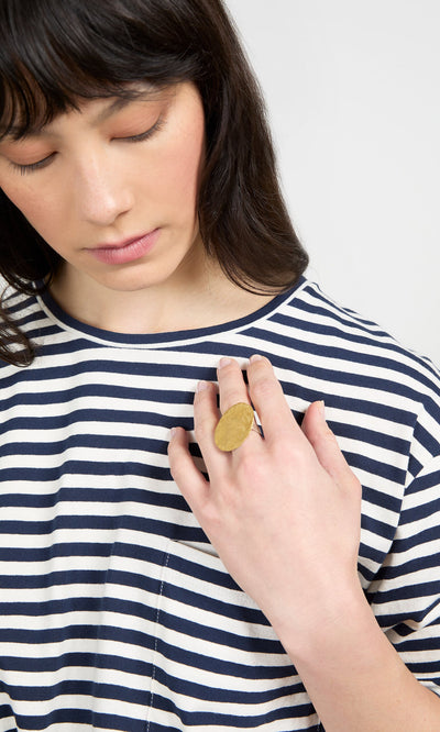 Plümo- A woman in a striped shirt looks down, showing off a Brass Pebble Ring from handmade jewellery on her hand.