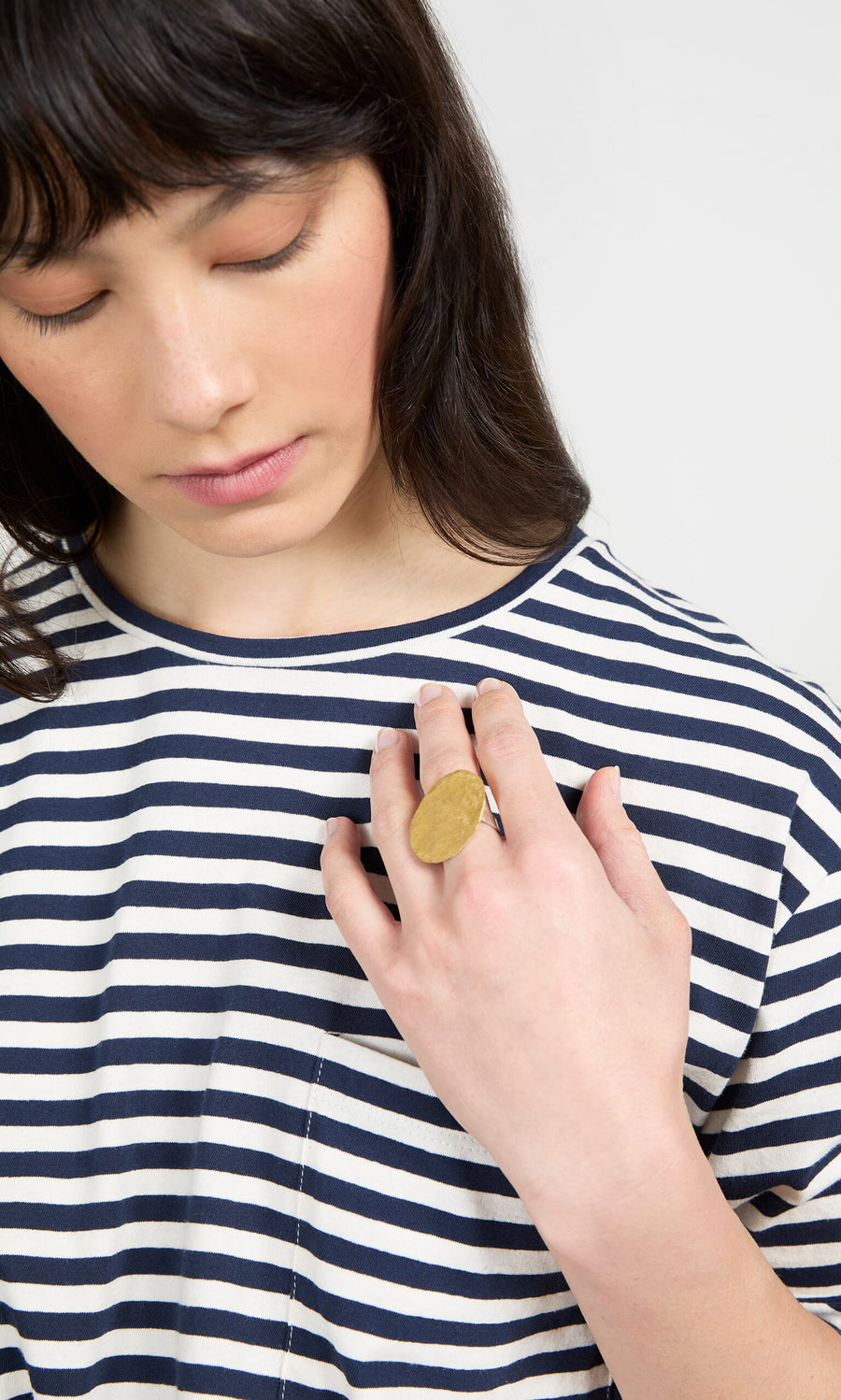 Plümo- A woman in a striped shirt looks down, showing off a Brass Pebble Ring from handmade jewellery on her hand.