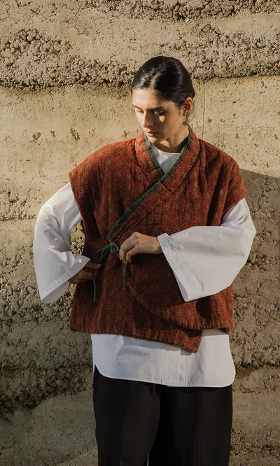 Plümo- Person in a red, block-printed Ansel Wrap Jacket ties the sash against a textured earth-toned wall.
