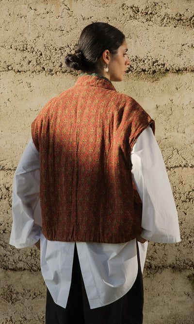 Plümo- Person stands with back to camera in an Ansel Wrap Jacket over a white shirt, against a textured wall.