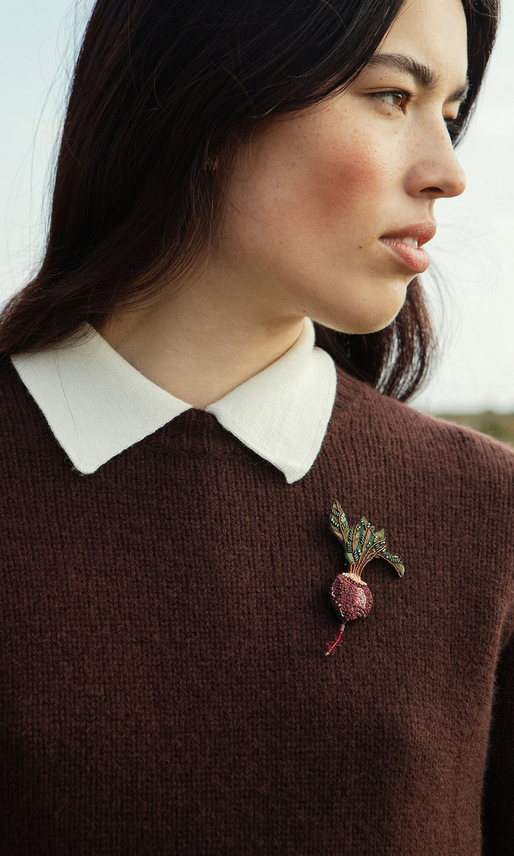 Plümo- Woman in the Bancroft Jumper, a supersoft merino wool sweater with white collar and beet brooch, looking to the side.