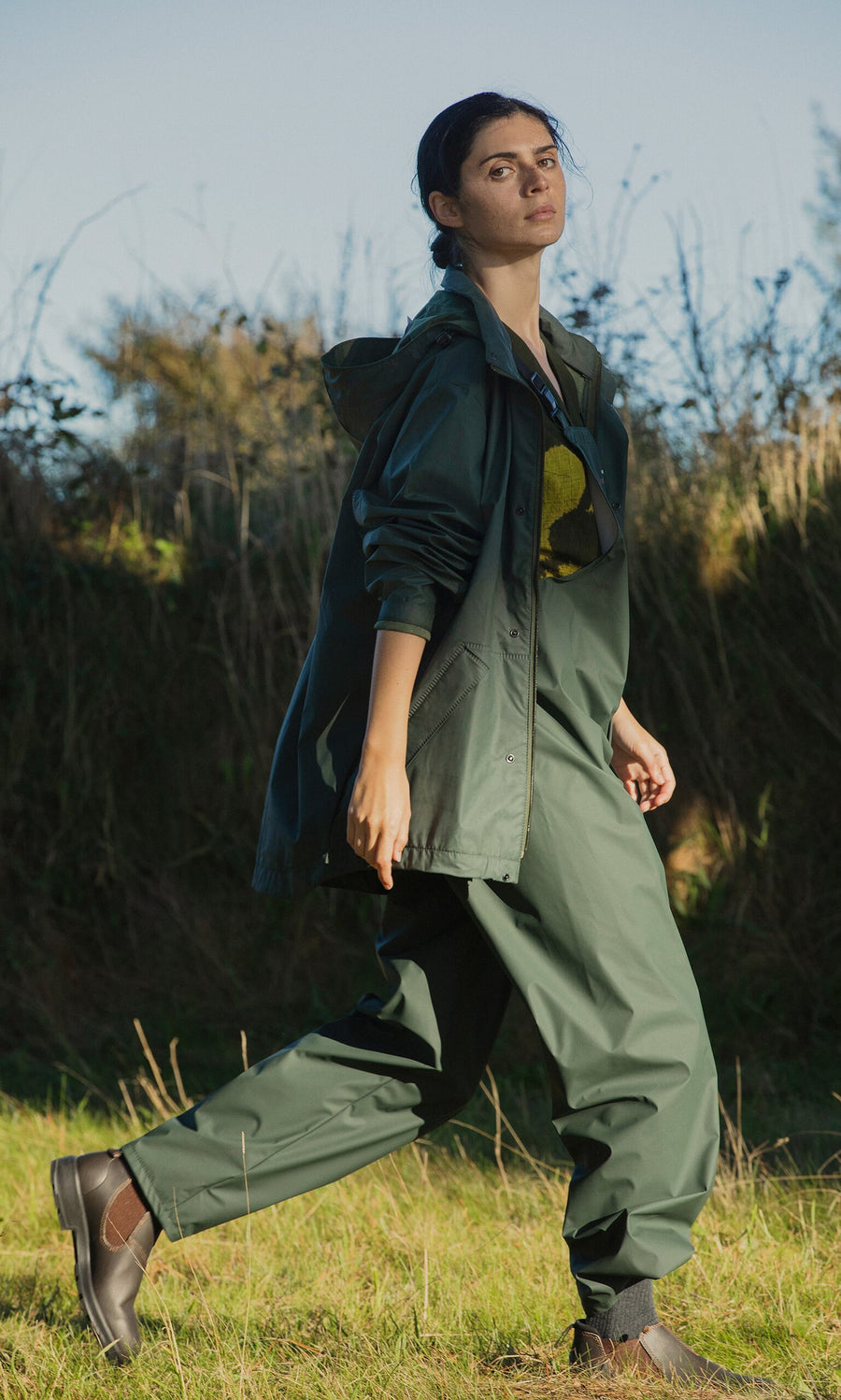 Plümo- Person in Land Dungarees walking on grass, with trees and a clear blue sky in the background.