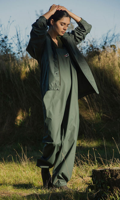 Plümo- A person in a Berghart Raincoat stands on grass with hands raised, sunlight and plants behind them.