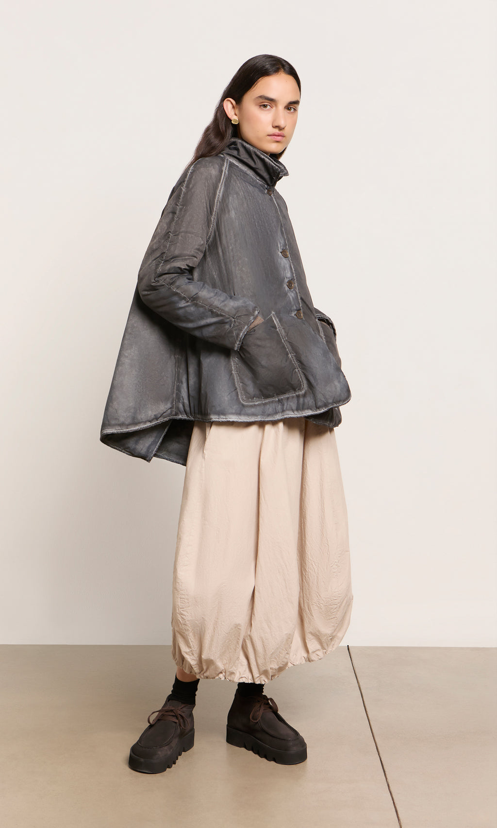 Plümo  Person in a Black Pepper Jacket and beige balloon pants stands on a light floor with neutral background.