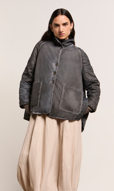 Plümo  Person wearing a Black Pepper Jacket with large pockets and a beige skirt, standing against a plain background.