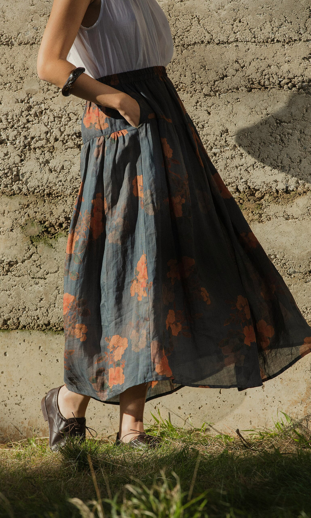 Plümo- Someone wears the Bloom Skirt with a white top and brown shoes, standing outdoors with one hand in their pocket.