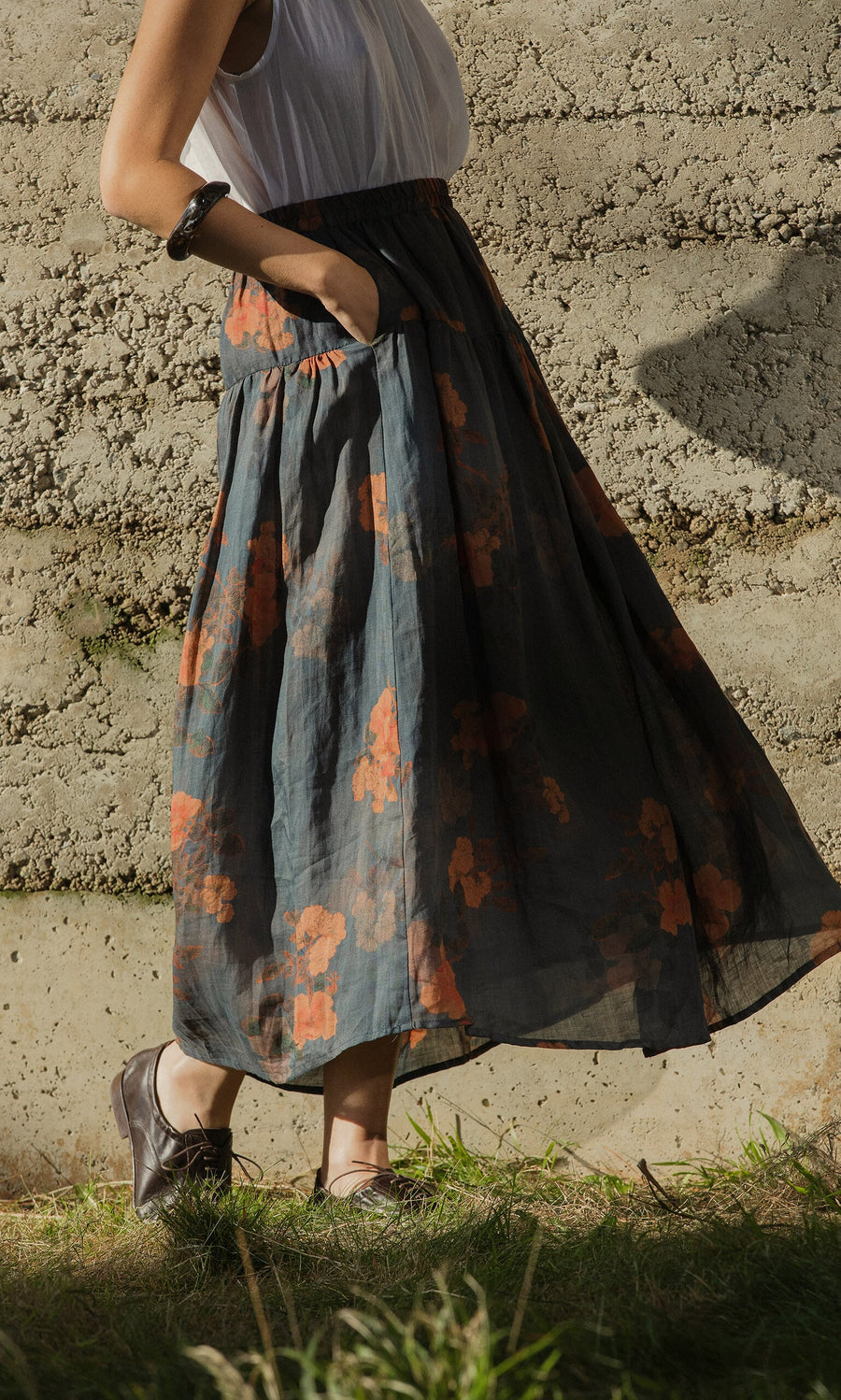 Plümo- Someone wears the Bloom Skirt with a white top and brown shoes, standing outdoors with one hand in their pocket.