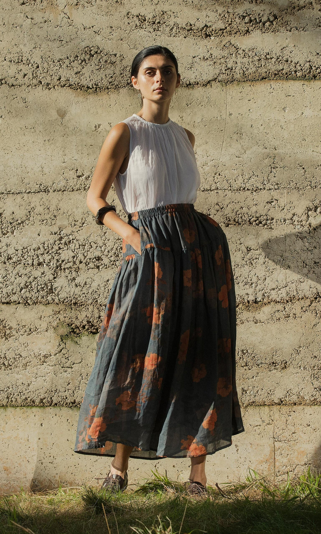 Plümo- Woman outdoors wearing the Bloom Skirt, a grey floral tiered skirt with pockets and an elasticated waist, and a white top.