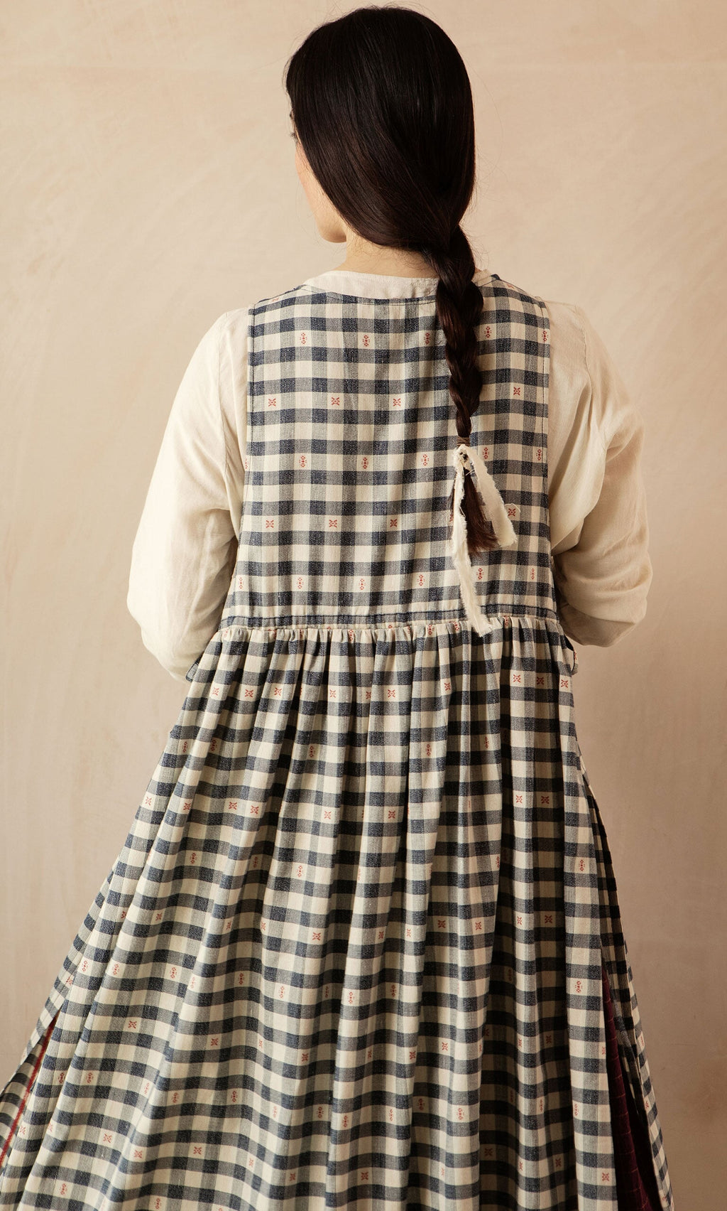 Plümo- Woman with long dark braid in the OMalley Apron Dress, featuring large pockets, seen from behind against a neutral backdrop.
