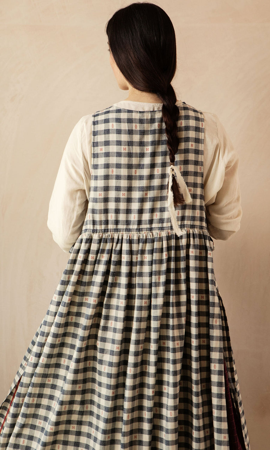 Plümo- Woman with long dark braid in the OMalley Apron Dress, featuring large pockets, seen from behind against a neutral backdrop.