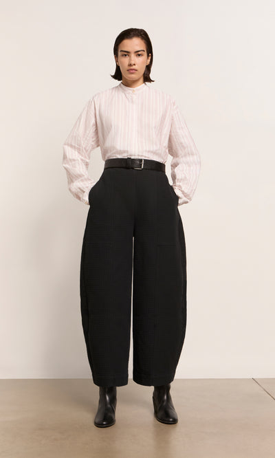 Plümo  A person wears a light striped shirt, Calow Pants - Coal with a wide black belt, and black boots against a plain background.