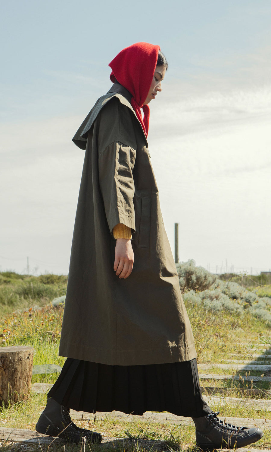 Plümo- Wearing a Cape Collar, a person walks outdoors on a sunny day, grass and sky in the background.