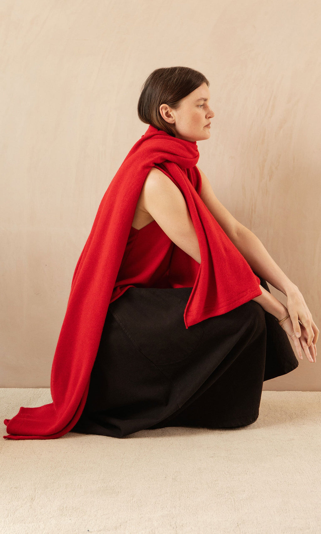 Plümo- A person in a supersoft red Stella Tank and black skirt sits sideways against a beige background.
