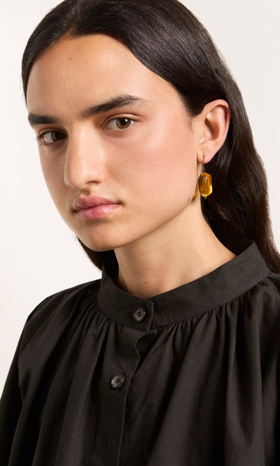 Plümo  Long-haired person wears a black top and Amber Glass Earrings, looking at the camera.