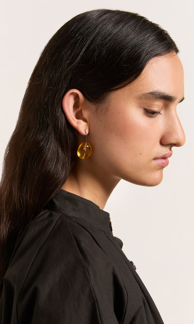 Plümo  Profile of woman with long dark hair wearing Amber Glass Earrings, featuring lightweight, amber-toned stones.