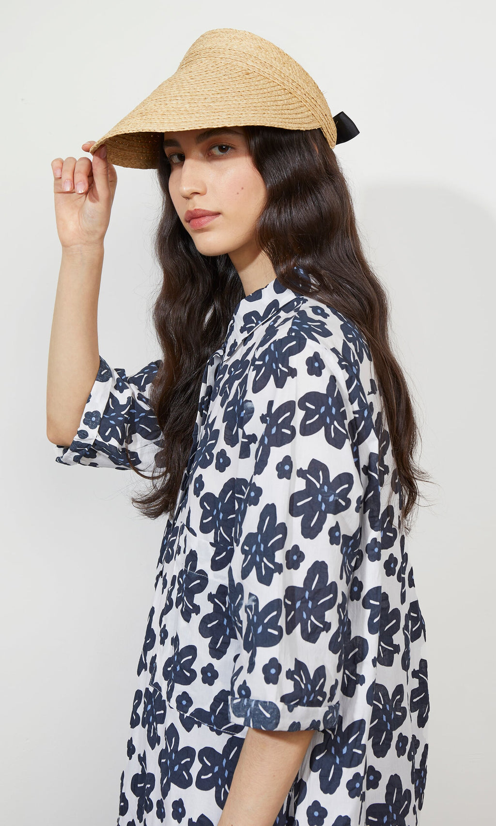 Plümo- Woman wears the Claude Sun Visor, a raffia sun visor with adjustable elastic band, paired with a floral dress.