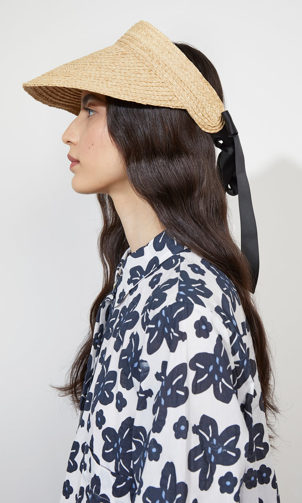 Plümo- Woman in profile wears the Claude Sun Visor, featuring black ribbon, elastic band, and a bold navy floral blouse.