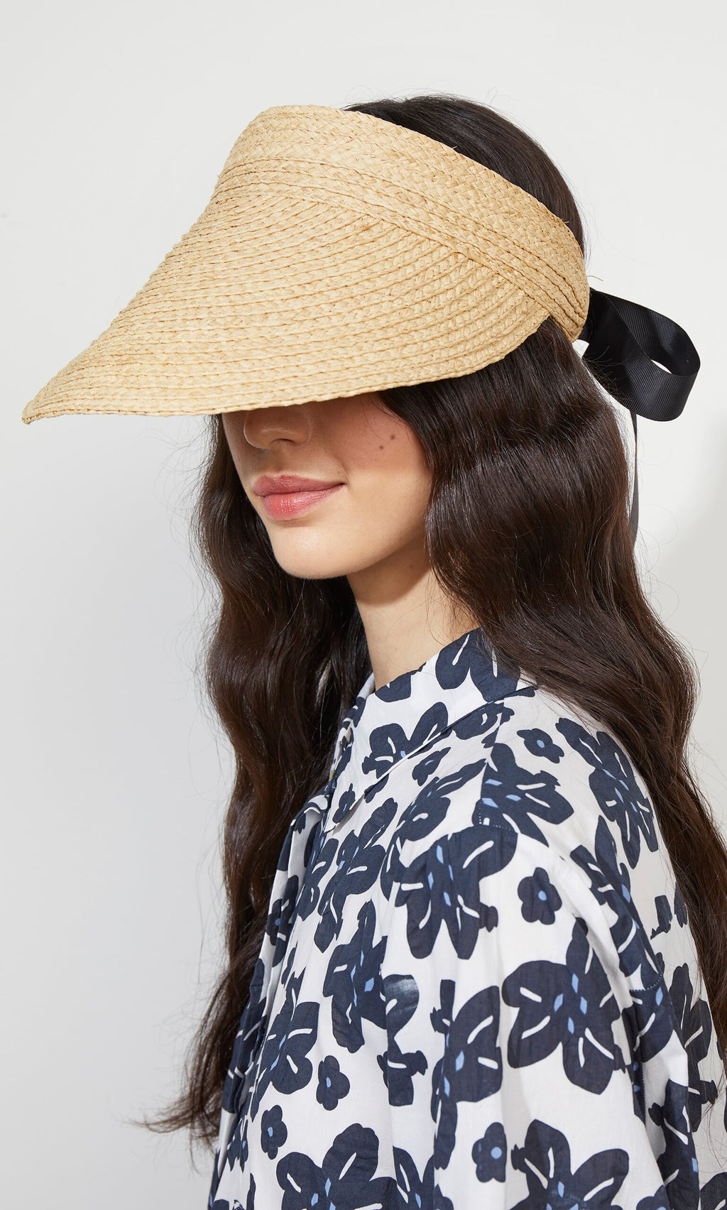 Plümo- Woman with long dark hair wears the Claude Sun Visor with black ribbon and elastic band, plus a dark floral shirt.