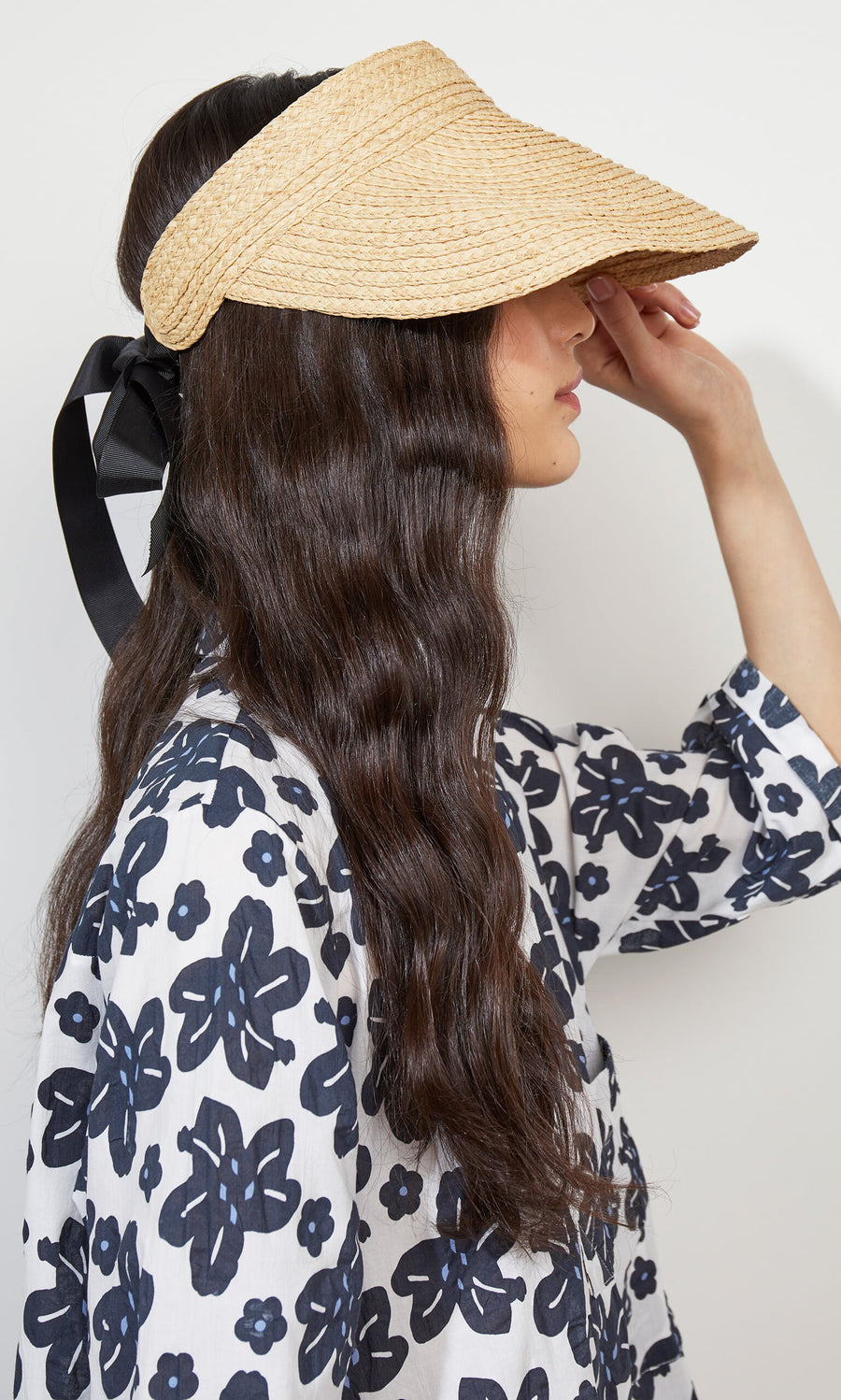Plümo- Woman wears the Claude Sun Visor—raffia with black ribbon and adjustable elasticated band—shown from the side.