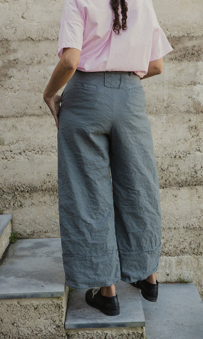 Plümo- Person on steps from behind wearing a pink shirt, Cora Grey Pants, and black shoes.