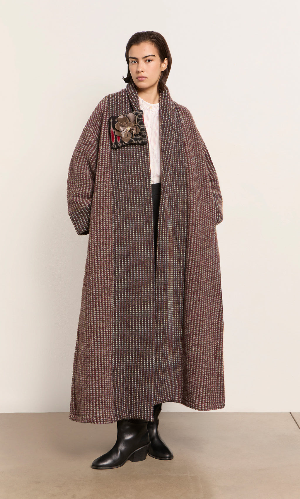 Plümo  A person in a Cordova Coat, white shirt, and black pants stands by a light wall; coat made in Italy.