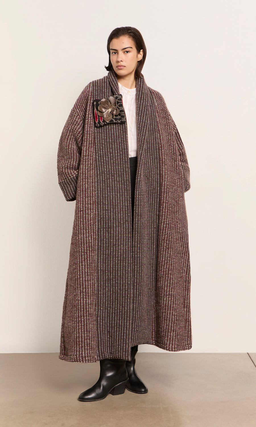 Plümo  A person in a Cordova Coat, white shirt, and black pants stands by a light wall; coat made in Italy.