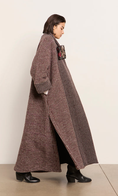 Plümo  Person in a Cordova Coat and black boots, with a scarf, standing sideways against a plain indoor wall.