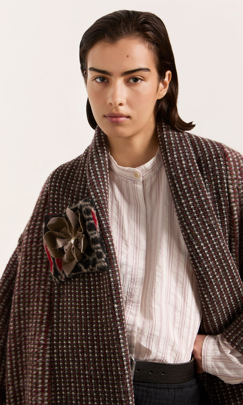 Plümo  Model wears the Cordova Coat with a detachable corsage over a white shirt, gazing directly at the camera.
