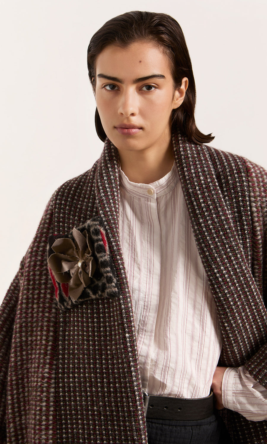 Plümo  Model wears the Cordova Coat with a detachable corsage over a white shirt, gazing directly at the camera.