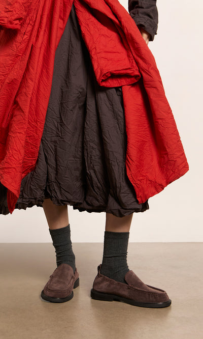 Plümo  Person wearing a red and brown wrinkled skirt, gray socks, and Dobin Loafers with cushioned insole on a gray floor.