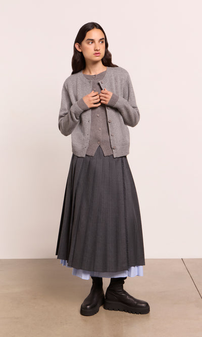 Plümo  Person in a Grey Melange Cardigan, long pleated skirt, black boots, on a light-colored floor.