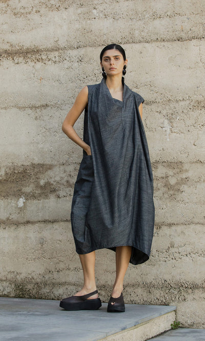 Plümo- A woman in the Emi Dress and black platform shoes stands against a textured concrete wall.