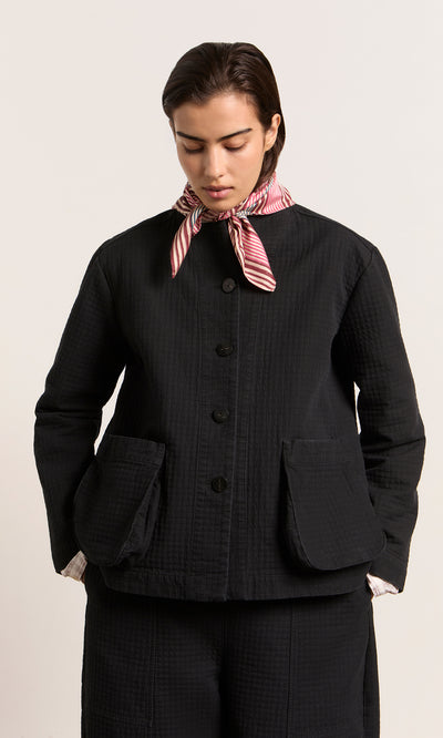Plümo  Person wearing the Envoy Jacket - Coal, matching pants, and a red-and-white striped scarf, looking down.