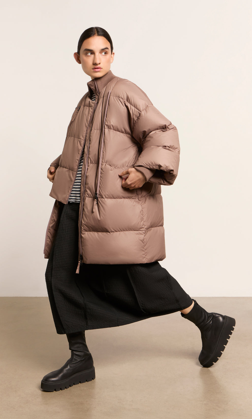Plümo  Person wearing a Firth Puffer Coat, black wide-leg pants, and chunky boots, walking indoors.