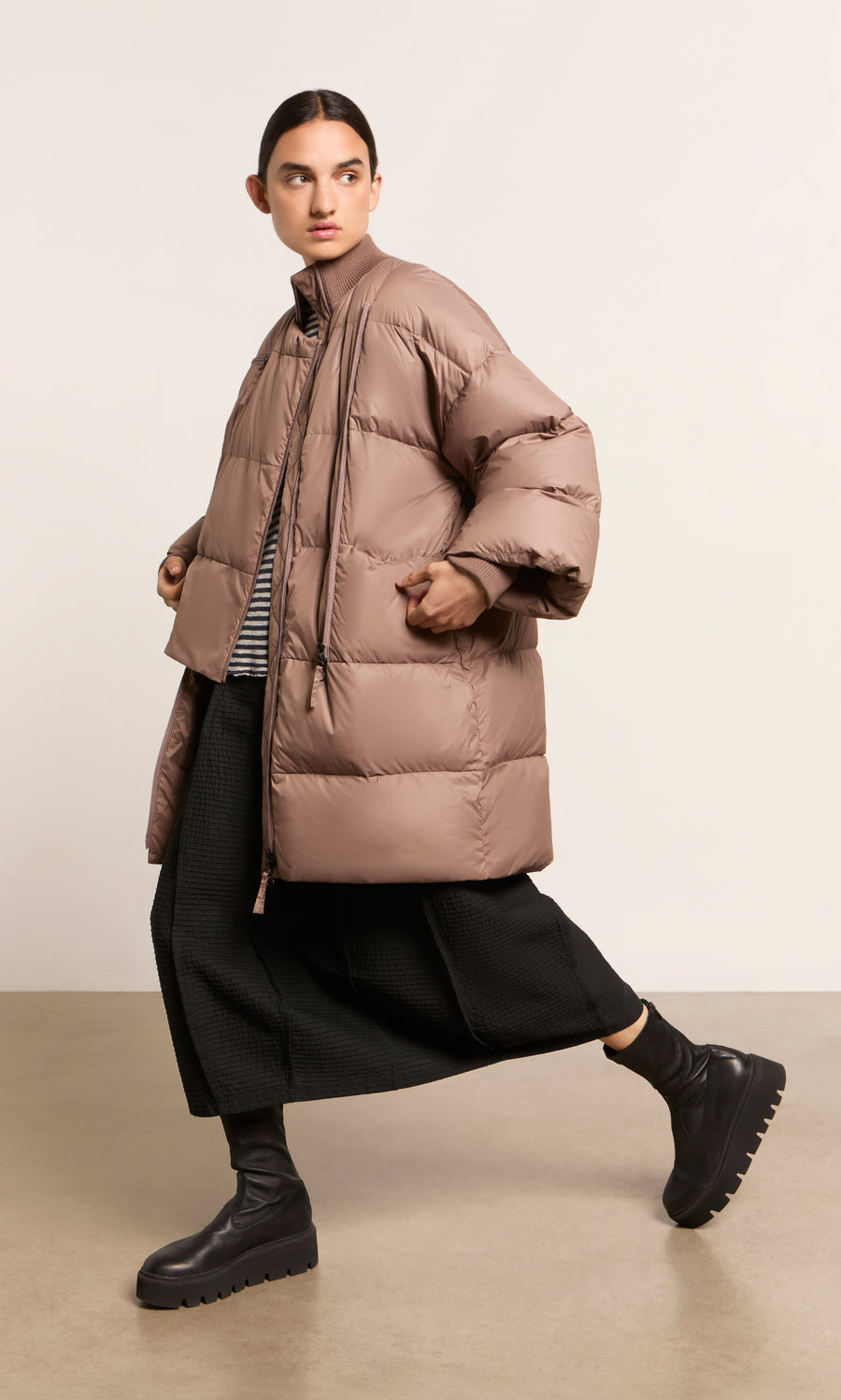 Plümo  Person wearing a Firth Puffer Coat, black wide-leg pants, and chunky boots, walking indoors.