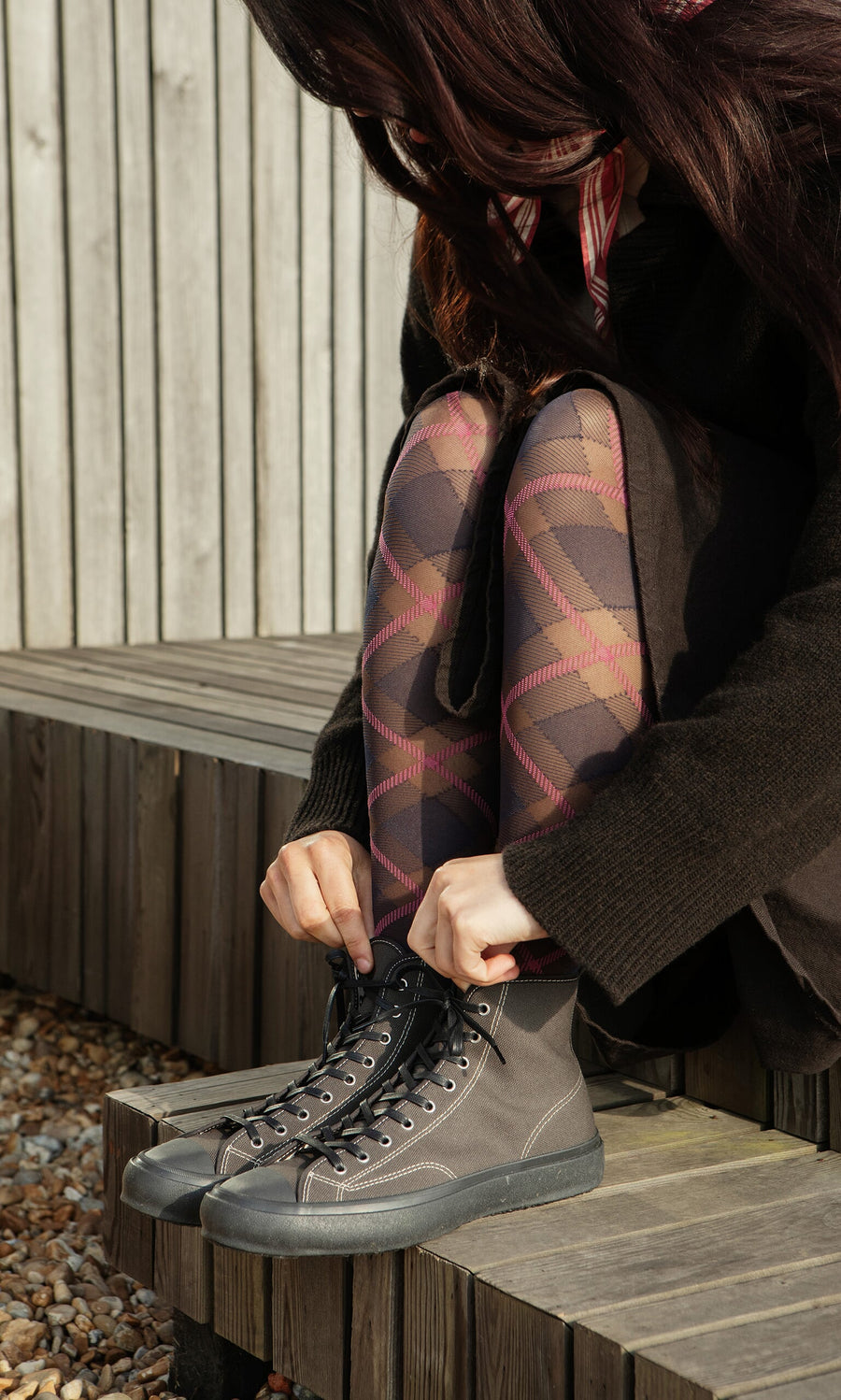 Plümo- Person tying the laces of High Top Trainers - Charcoal while wearing patterned tights on a wooden bench.